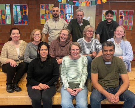 Das Pflegeteam, insgesamt 9 Personen, sitzen in drei Reihen auf den B&auml;nken der Aula